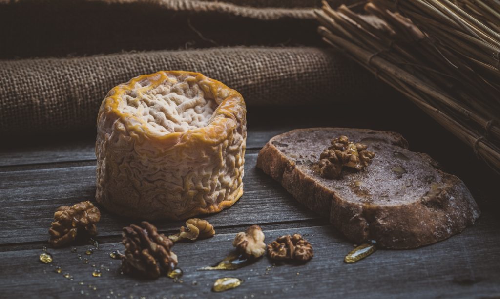 rustic alpine cheese on a board with bread and walnuts